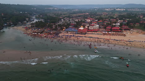 drone flying around the baga beach full of people, sunny evening in goa, india