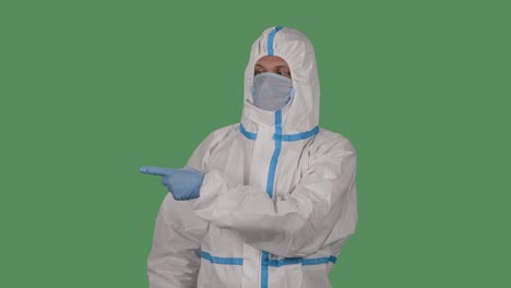 portrait of a man in a protective suit and medical mask looks at the camera and points his fingers to the side, up and down. green screen, chroma key. slow motion. close up