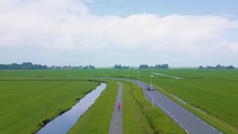 Cute-girl-in-pink-biking-on-bike-path-in-empty-flat-Dutch-green-polder