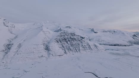 Aerial-landscape-view-over-Skaftafellsjokull-glacier-surrounding-mountains,-in-Iceland,-covered-in-snow,-during-sunset