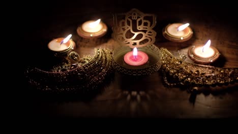 inclinarse hacia la adoración de la boda nupcial dorada ornamentada y las joyas ceremoniales con las bendiciones de lord ganesha escultura recortada entre las velas de diya rojas para diwali, el festival hindú de las luces.