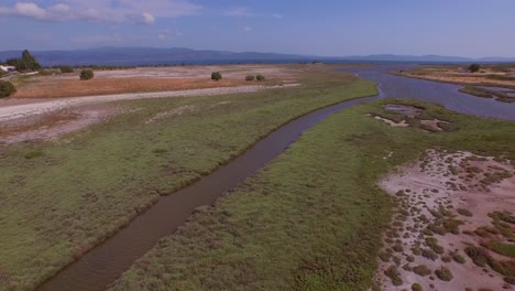 Aerial:-A-river-delta-with-a-road-bridge-passing-through-and-some-agricultural-buildings