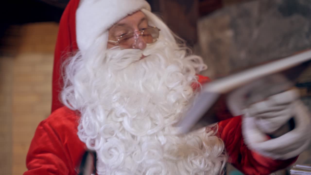 Portrait of Santa with a book. Santa Claus with white beard in eyeglasses looking into the magic book indoors. Close-up. Christmas time.
