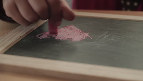 a child draws a pink heart on a slate with chalk as the camera tracks right