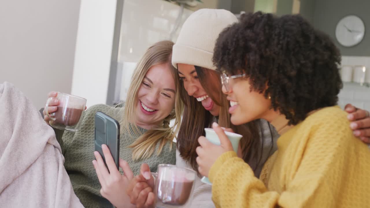 felices adolescentes diversas amigas bebiendo café y usando el teléfono inteligente en casa, cámara lenta