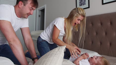 mom and father tickling her child. people, family, fun and morning concept - happy child with parents tickling in bed at home. happy family spending time together in bedtime playing and hugging