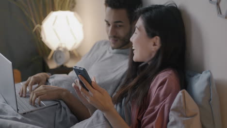 couple working on laptop and phone in bed at night