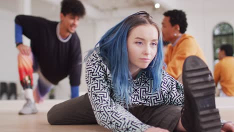 caucasian female dancer stretching with diverse colleagues in dance studio, slow motion