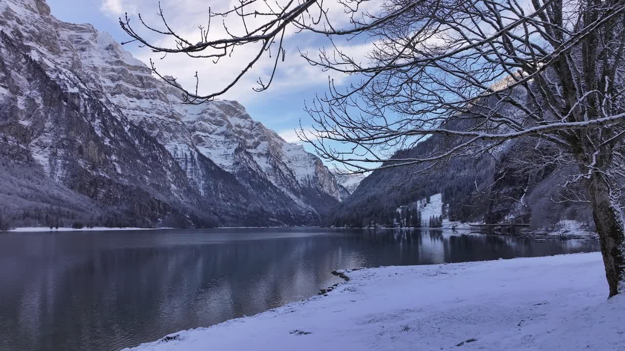 A serene winter wonderland at Lake Klöntalersee, Switzerland, showcasing the enchanting beauty of snow-covered landscapes and the tranquil atmosphere of the season.
