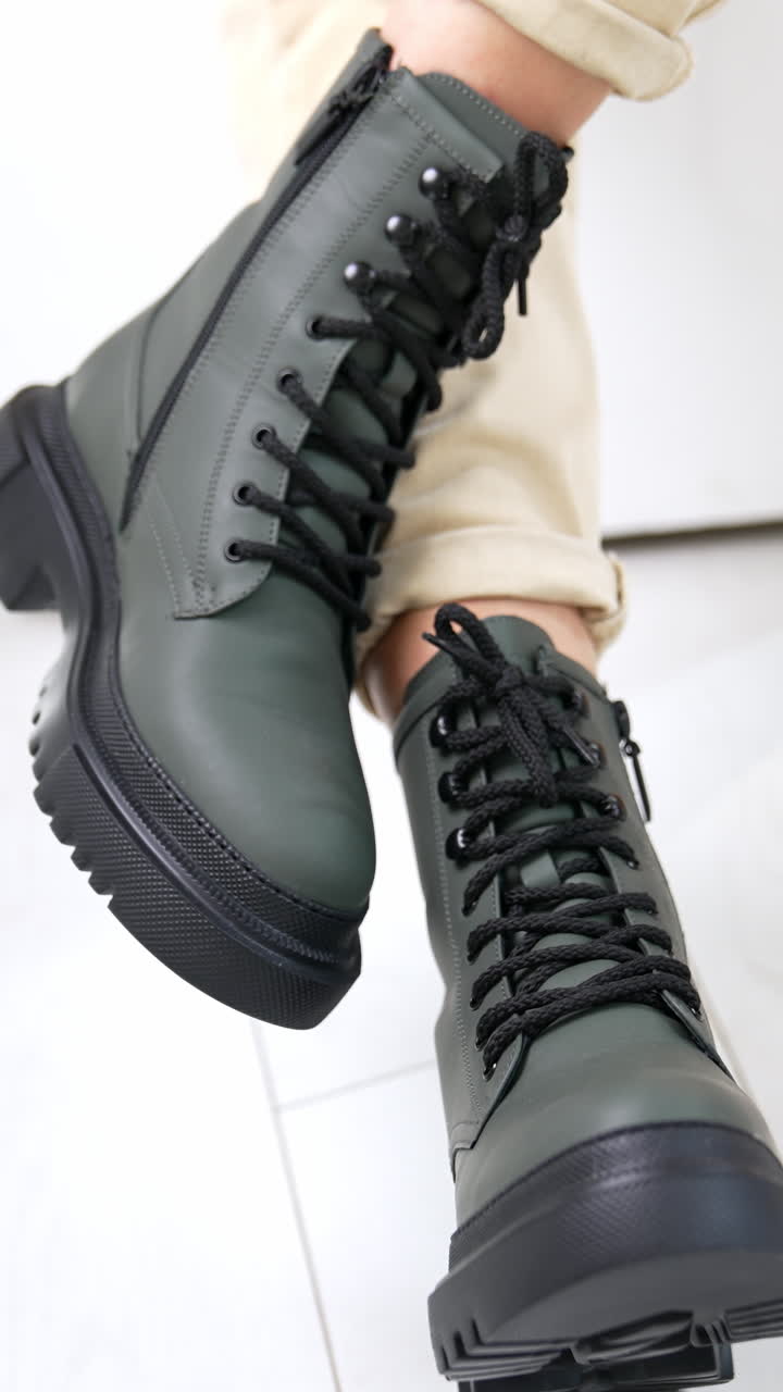 Woman sitting in studio demonstrating grey boots on tractor soles. Beautiful modern footwear at white backdrop. Close up. Vertical video