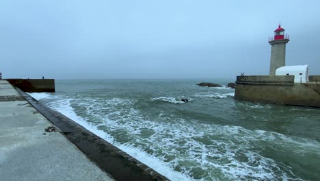 cámara lenta de olas tormentosas que se estrellan contra la pared en el puerto de oporto con faro durante el día nublado y oscuro