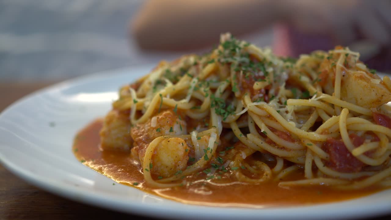 A little girl eats tomato seafood spaghetti in a restaurant. The subject is on the right.