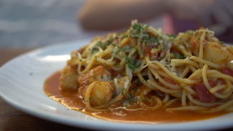 a little girl eats tomato seafood spaghetti in a restaurant. the subject is on the right.