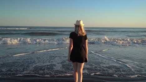 attractive woman in summer dress walking towards sandy beach with rolling waves at monte hermoso, buenos aires, argentina