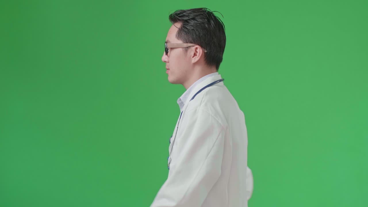 The Side View Of Asian Doctor With Stethoscope Wearing Glasses And White Coat Walking On Green Screen Chroma Key.
