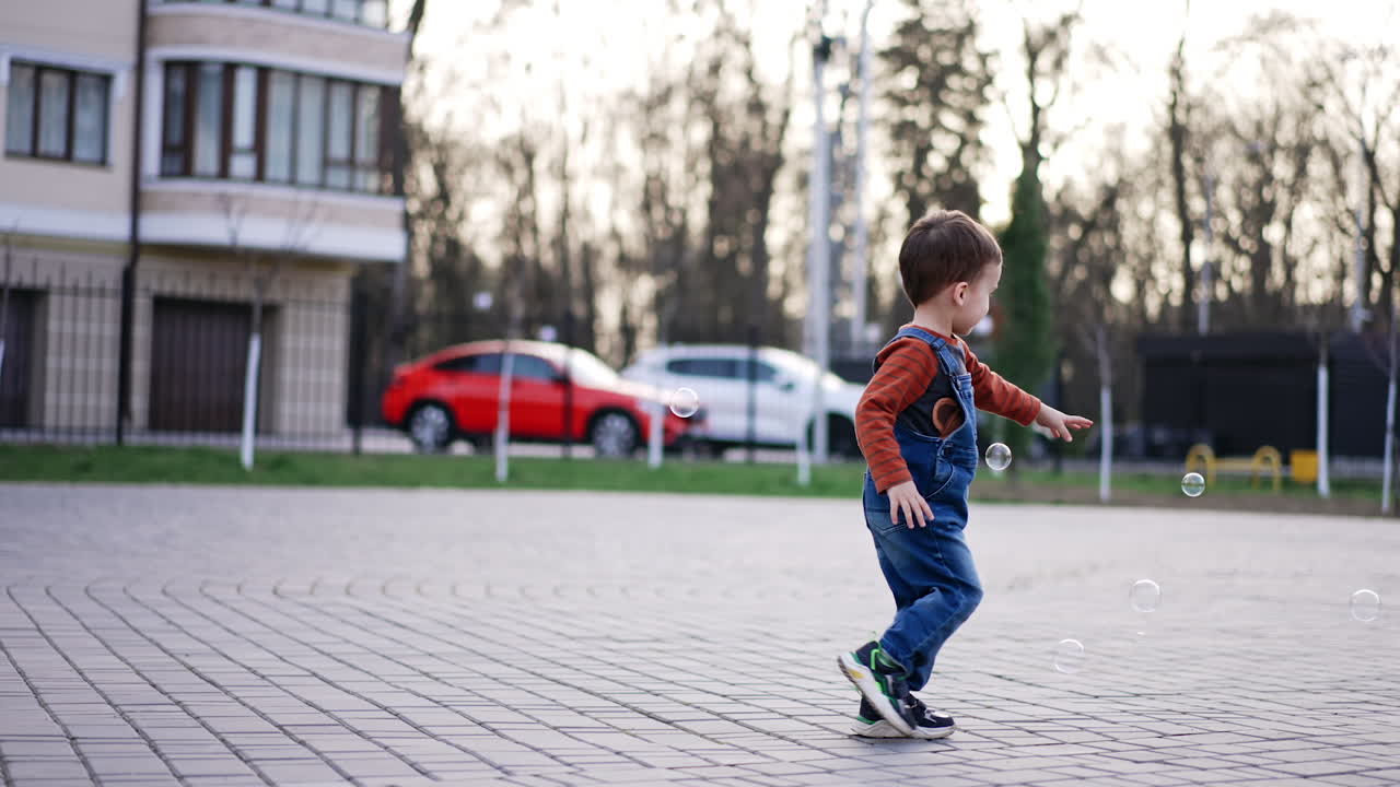 Caucasian toddler runs to catch the soap bubbles. Happy active baby boy having fun outdoors.