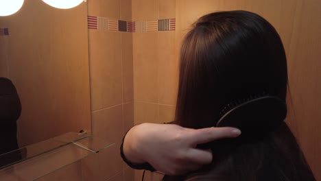 Young-brunette-woman-brushing-hair-in-bathroom-mirror,-Slowmo-Closeup-Circle-Pan