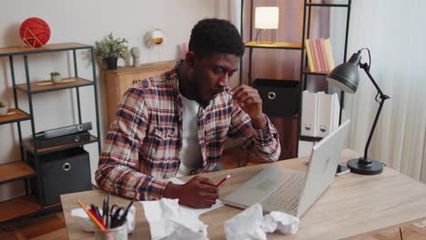 tired man at home office falling asleep on table with laptop computer, crumpled sheets of paper