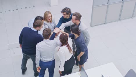 trabalhadores de escritório fazendo exercício de team building empilhando as mãos juntos no espírito unificador de criatividade e causa comum. oito pessoas bem-sucedidas aplaudindo juntos. fotografia de alto ângulo em escritório moderno