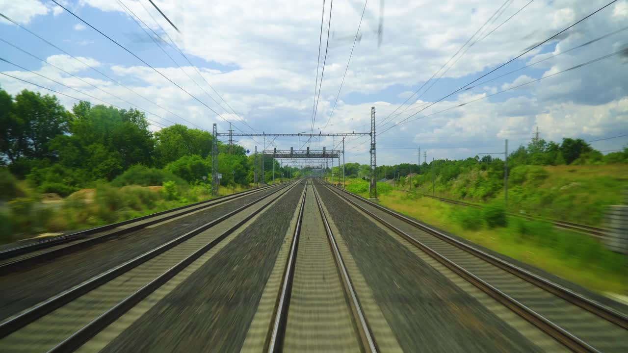 배경에는 전력선과 나무가 있는 열차 트랙. 트랙은 푸른 풀로 둘러싸여 있으며, 트랙의 길이를 따라 하 ⁇  구름이  ⁇ 어져 있습니다.