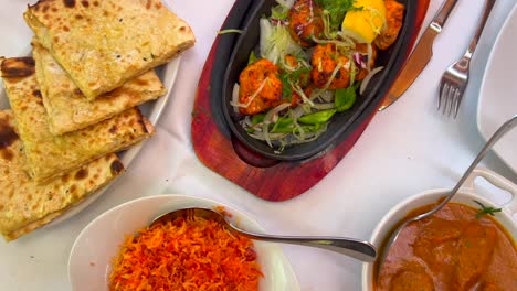 traditional indian tandoori chicken with onions on a very hot plate, butter chicken, cheese naan bread and coconut rice in a restaurant, authentic asian food, 4k top shot