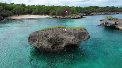 Bandera-De-República-Dominicana-Ondeando-Sobre-Una-Roca-Rodeada-Por-El-Mar-Caribe