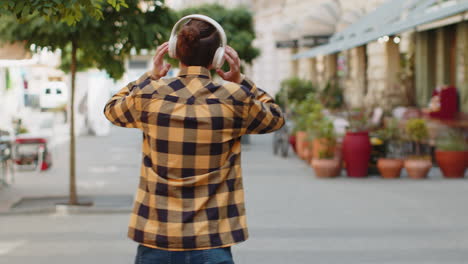 Vista-Trasera-De-Un-Turista-Feliz-Y-Relajado-Con-Auriculares-Inalámbricos-Escuchando-Música-Caminando-Por-Las-Calles-De-La-Ciudad