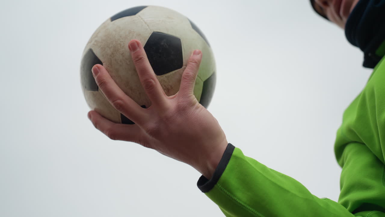 persona exultante con equipamiento deportivo, competidor levantando con alegría una pelota bajo cielos nubosos, individuo mostrando con entusiasmo un momento de victoria con accesorios deportivos contra un cielo gris sombrío