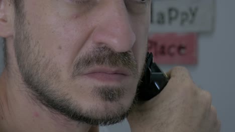 a caucasian middle-aged guy is trimming his beard with an electric shaver to have a handsome hair length