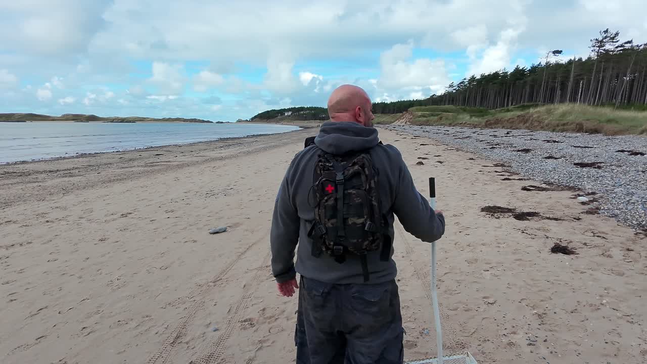 웨일즈 해변에서 모래 스쿠프를 들고 는 남성의 뒤를 따라 이른 아침 휴식을 취합니다.