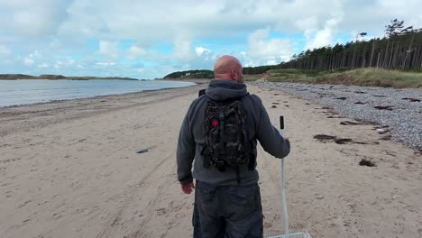 following male walking with sand scoop on welsh beach for early morning relaxation