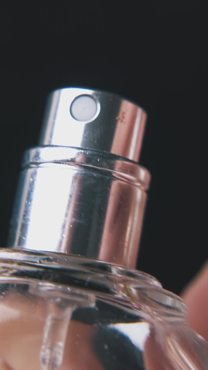 young man takes off plastic cap from women perfume water bottle on dark background extreme close view