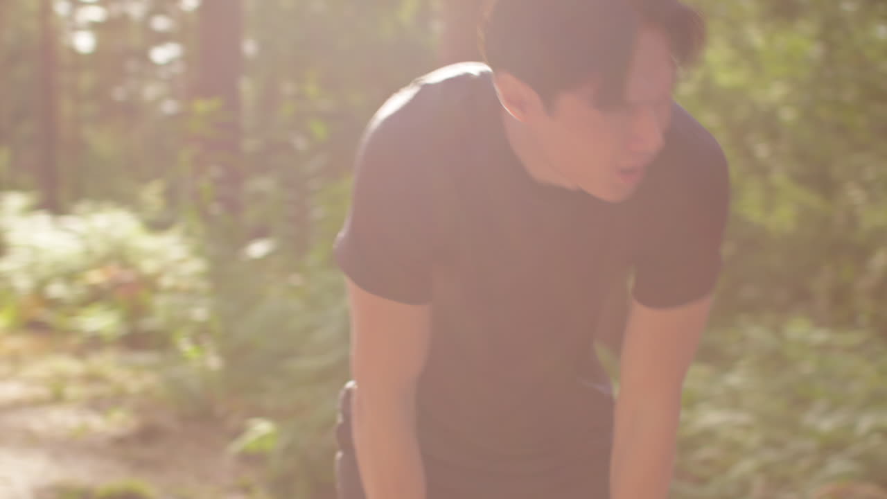 피곤한 중성인 남자가 야외에서 운동을 하고 숲을 가로질러 달리고 숨을 쉬기 위해 멈추고 실시간으로 습니다.