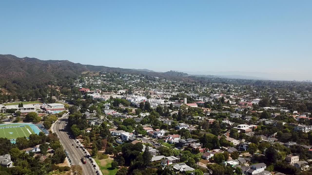 Aerial establishing shot of american highway in noble suburb district of Los Angeles in fall. Slow forward flight in pacific palisades. Exclusive houses and villas. Sunny day with blue sky in USA.