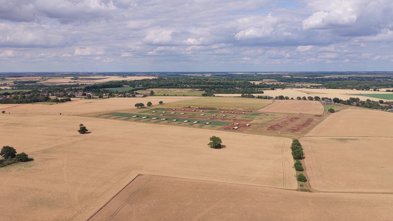 Champs dorés et secs pendant la saison des récoltes estivales, tandis que de lourdes machines agricoles récoltent des céréales sous un ciel bleu éclatant avec de légers nuages à travers le vaste paysage rural