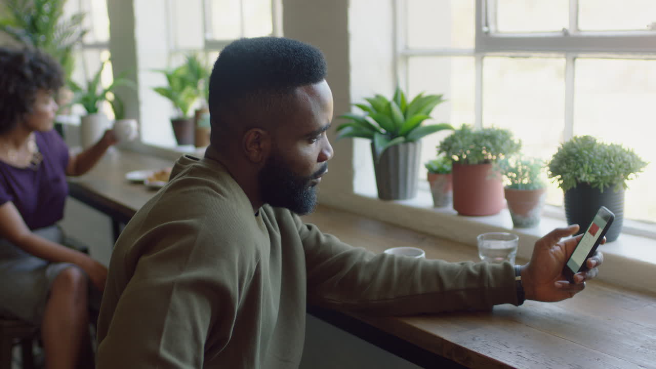 joven afroamericano usando un teléfono inteligente en un café navegando por mensajes en línea enviando mensajes de texto compartiendo estilo de vida en las redes sociales disfrutando del teléfono móvil