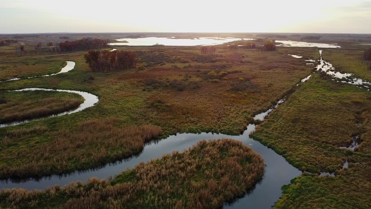 Un vasto paesaggio di zone umide che si estende verso il tramonto, con canali d'acqua serpeggianti