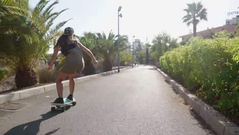 Die-Zeitlupe-Fängt-Den-Bezaubernden-Anblick-Eines-Jungen-Mädchens-Ein,-Das-Auf-Seinem-Longboard-Auf-Einer-Straße-In-Der-Nähe-Von-Palmen-Und-Dem-Strand-Fährt