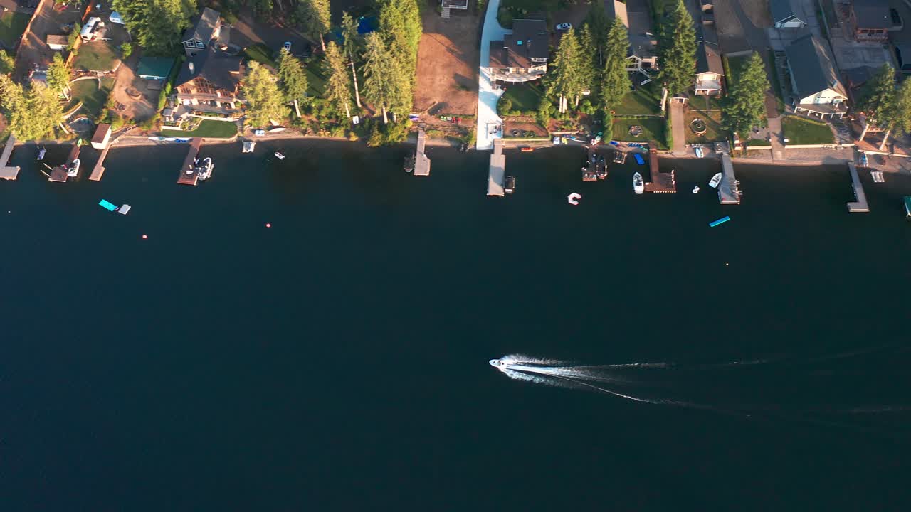 Bird's eye view tracking pan follows boat driving along backyard docks in beautiful lake, aerial