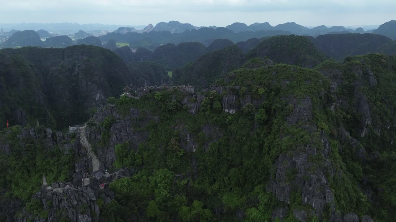 Drone zoom in on dramatic karst mountain covered in dense green vegetation in Ninh Binh region