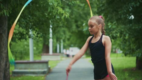 a young gymnast performs a captivating ribbon routine outdoors, showcasing grace and skill amidst a lush green park landscape, surrounded by nature