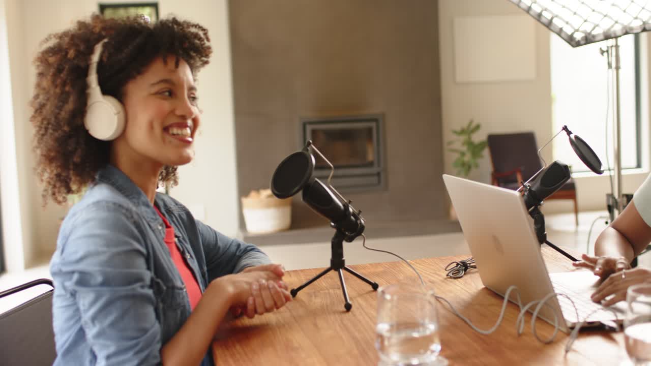 Conduttrici donne di varie etnie che digitano sul laptop, iniziano un podcast, parlano nei microfoni e ridono in uno studio casalingo
