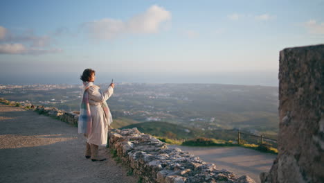 woman filming evening coastline in smartphone at scenic viewpoint. girl blogger