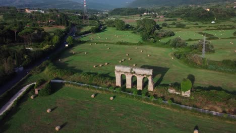 ancient roman aqueduct ruins in pastoral lazio landscape, italy, hay bales scattered in fields, aerial view