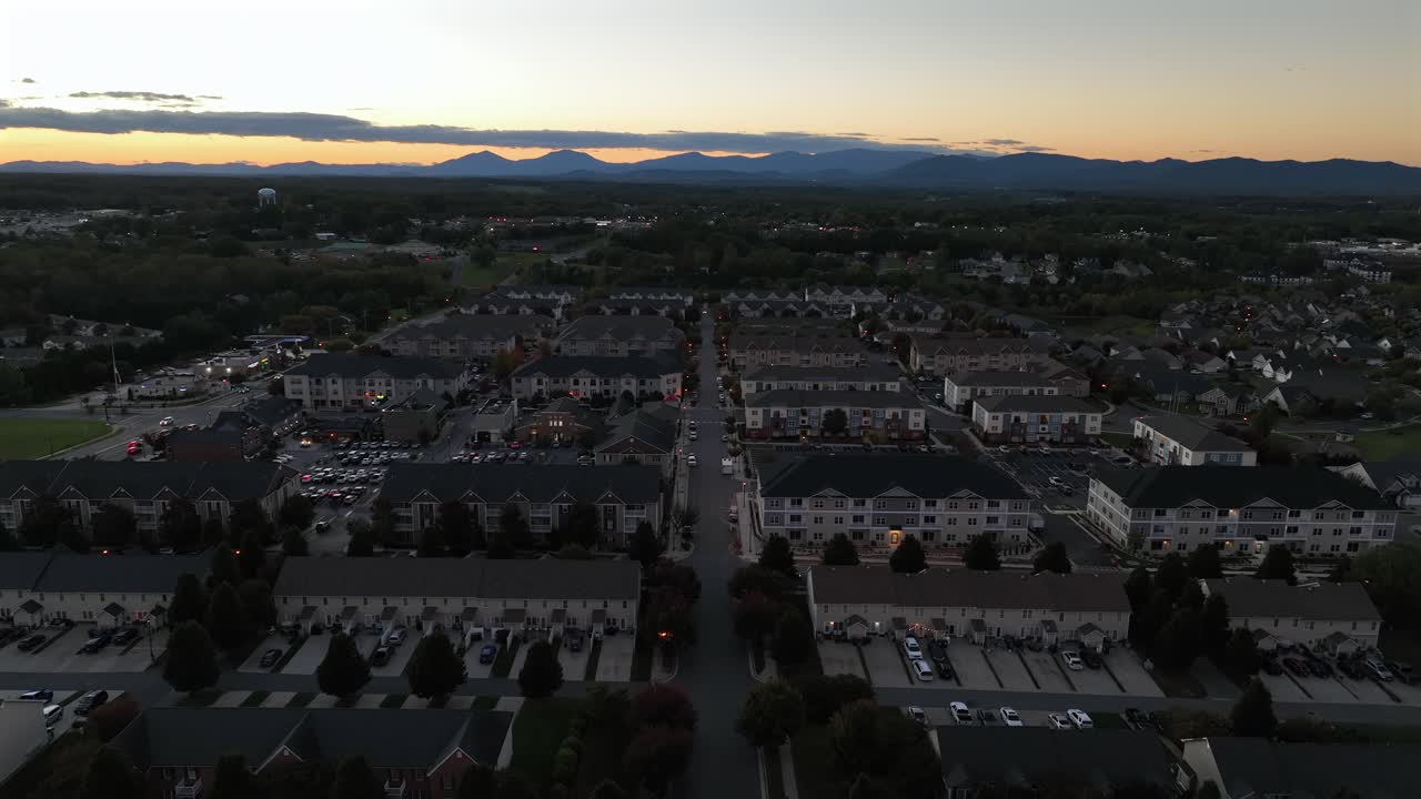 American suburban architecture with uniform townhouses, modern apartments and wide streets. Sunset light and distant mountain silhouettes in distance. Aerial wide shot