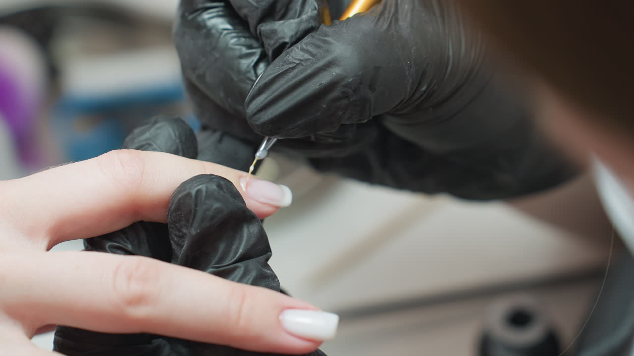 Closeup of nail technician wearing black gloves using tiny precision brush to carefully apply acrylic on client's nail, demonstrating skill and concentration during salon manicure treatment process