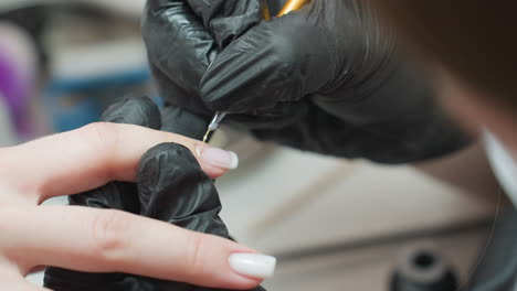 closeup of nail technician wearing black gloves using tiny precision brush to carefully apply acrylic on client's nail, demonstrating skill and concentration during salon manicure treatment process