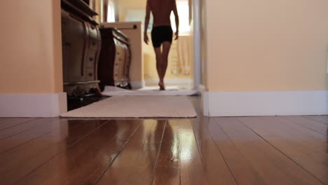 a man clad only in his underwear walks across a wooden floor and into the dressing room