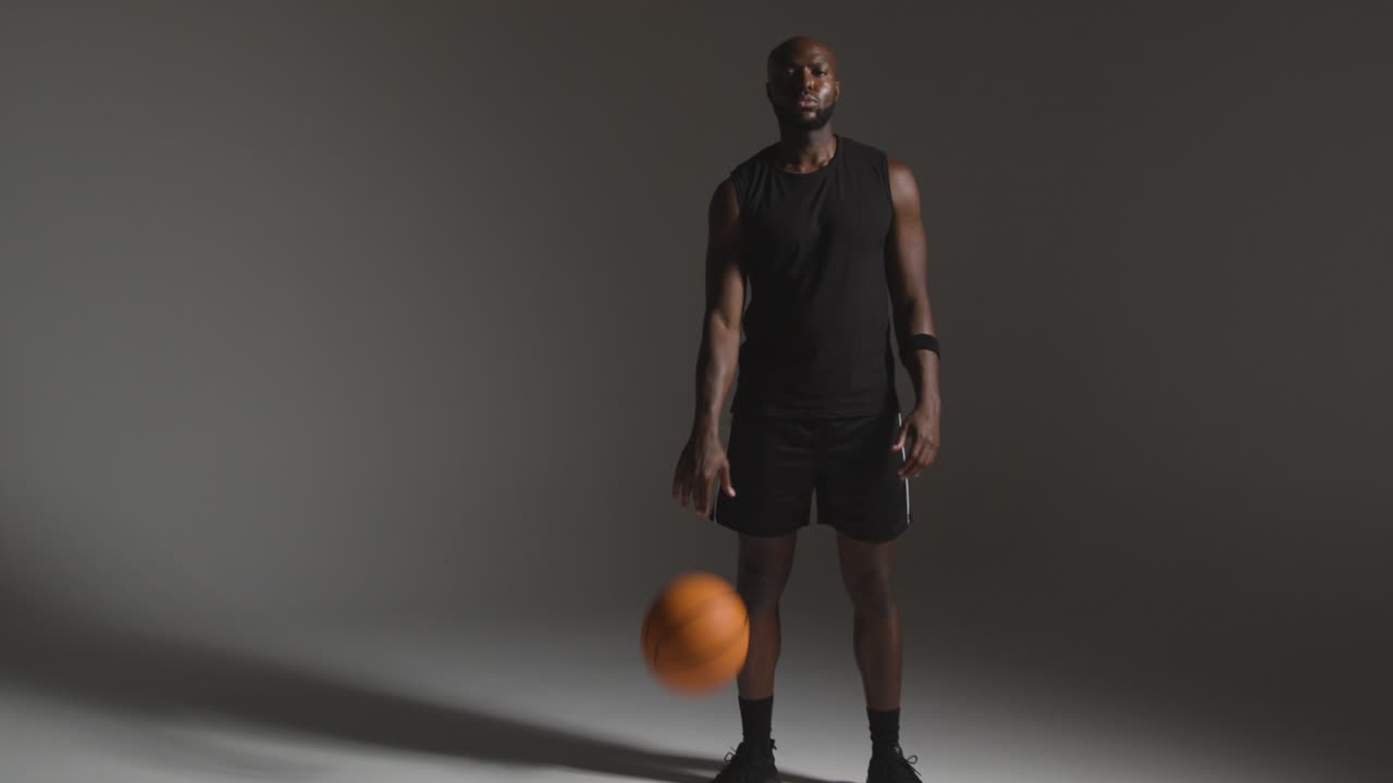 retrato de estudio de longitud completa de un jugador de baloncesto masculino driblando la pelota contra un fondo oscuro