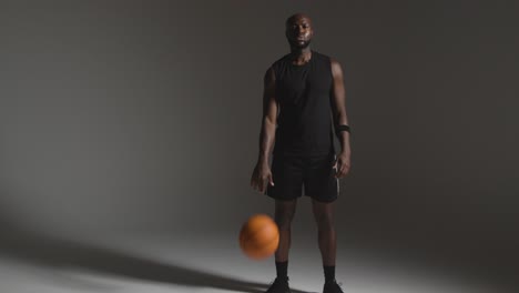 Studioporträt-In-Voller-Länge-Eines-Männlichen-Basketballspielers,-Der-Vor-Dunklem-Hintergrund-Einen-Ball-Dribbelt